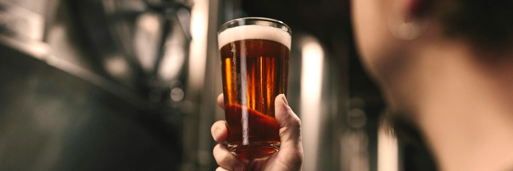 Glas mit bernsteinfarbenem Bier vor Braukesseln