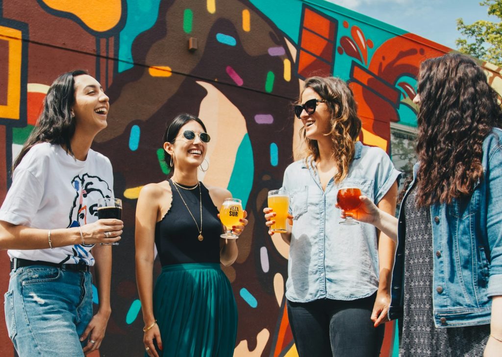 four women holding drinks while laughing together during daytime